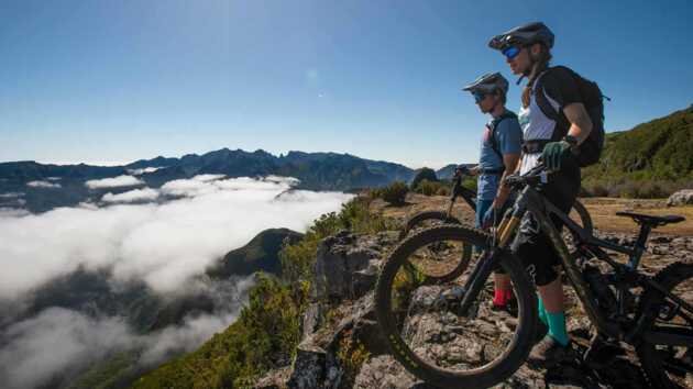 2 Mountainbiker stehen auf dem berg und blicken über die Wolken und über Madeira