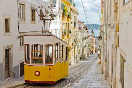 Bekannte, gelbe, historische Tram fährt durch die engen Gassen den Berg hinauf. Ein Muss in jedem Lissabon Urlaub