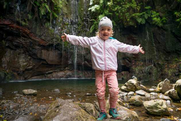 Mädchen steht vor einem Wasserfall auf Madeira, beide Arme ausgestreckt.