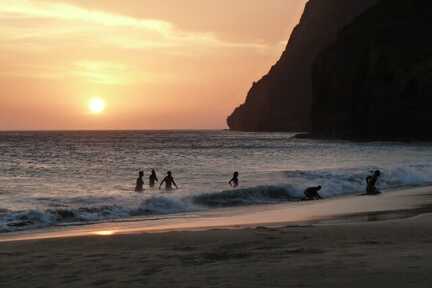 Menschen planschen im Wasser am Strand bei Sonnenuntergang.