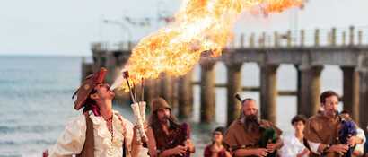 Ein als Seefahrer verkleideter Mann spuckt im Vordergrund Feuer und im Hintergrund stehen mehrere und spielen Dudelsack. Womöglich entstand dieses Bild beim Kolumbus Festival auf Porto Santo.