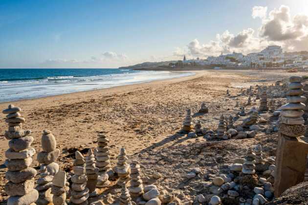 Langer, menschenleerer Strand mit aufgetürmten Steinchen im Vordergrund und Städtchen im Hintergrund