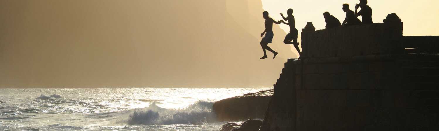 Junge Männer springen von Felsen ins Meer