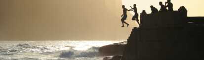 Junge Männer springen von Felsen ins Meer